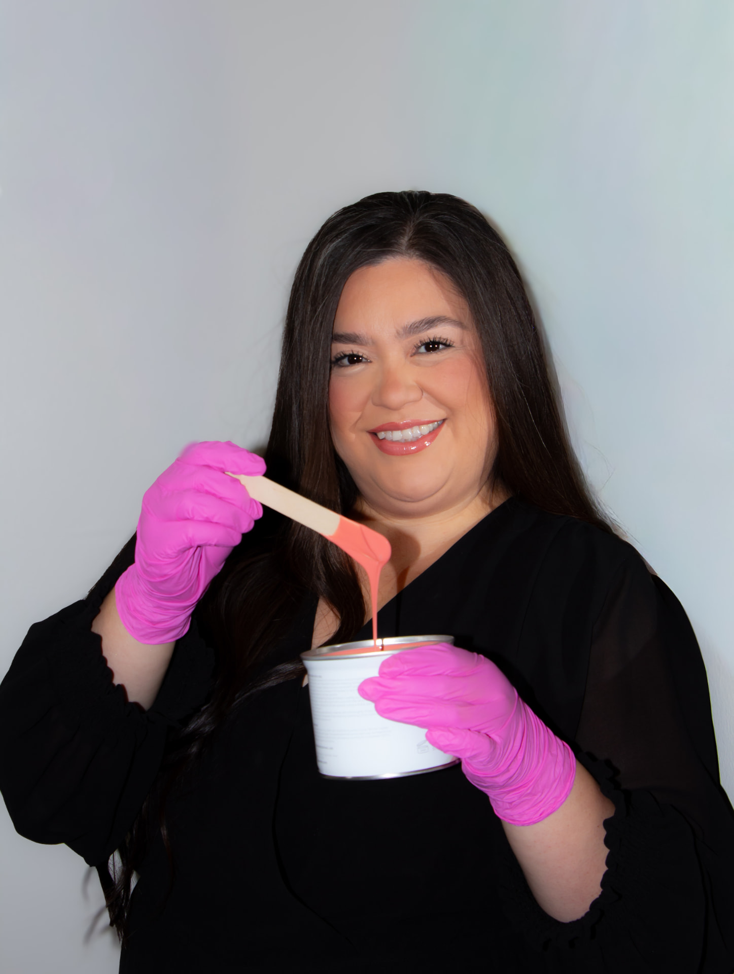Licensed esthetician Jaquie holding pink wax and a spatula at Eres Beauty Studio